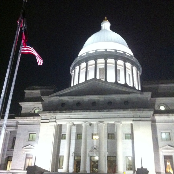The red, white and blue stand out against the night sky and limestone of the Arkansas State Capitol.